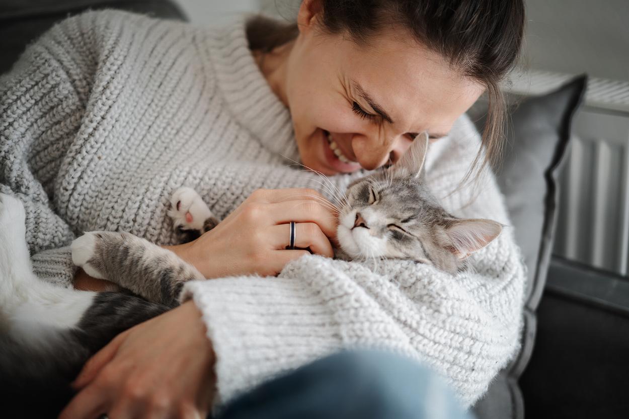 a lady in a sweater sitting on a sofa cuddling with a content cat