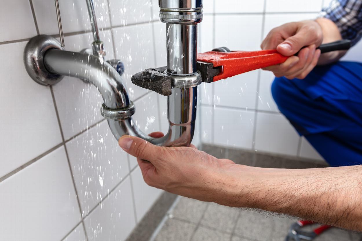 a person using a wrench fixing the leaking plumbing of a sink